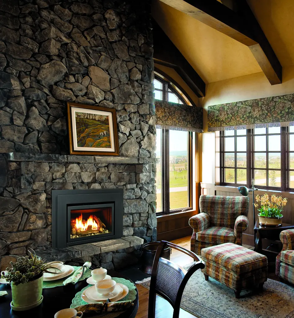 Ambiance de chalet de luxe avec un insert au gaz Enviro E33 installé dans une imposante cheminée en pierres des champs avec poutres de bois au plafond.