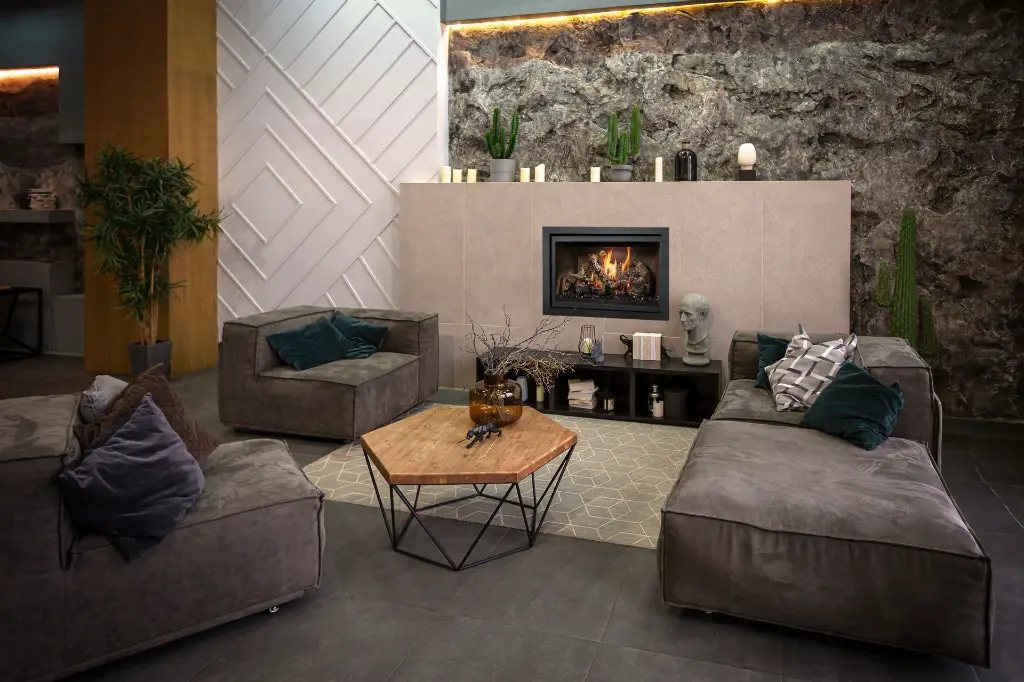 Ambiance masculine et contemporaine avec le foyer au gaz 564 TV 35K installé dans une structure en tuiles sur un mur de pierres naturelles brutes.