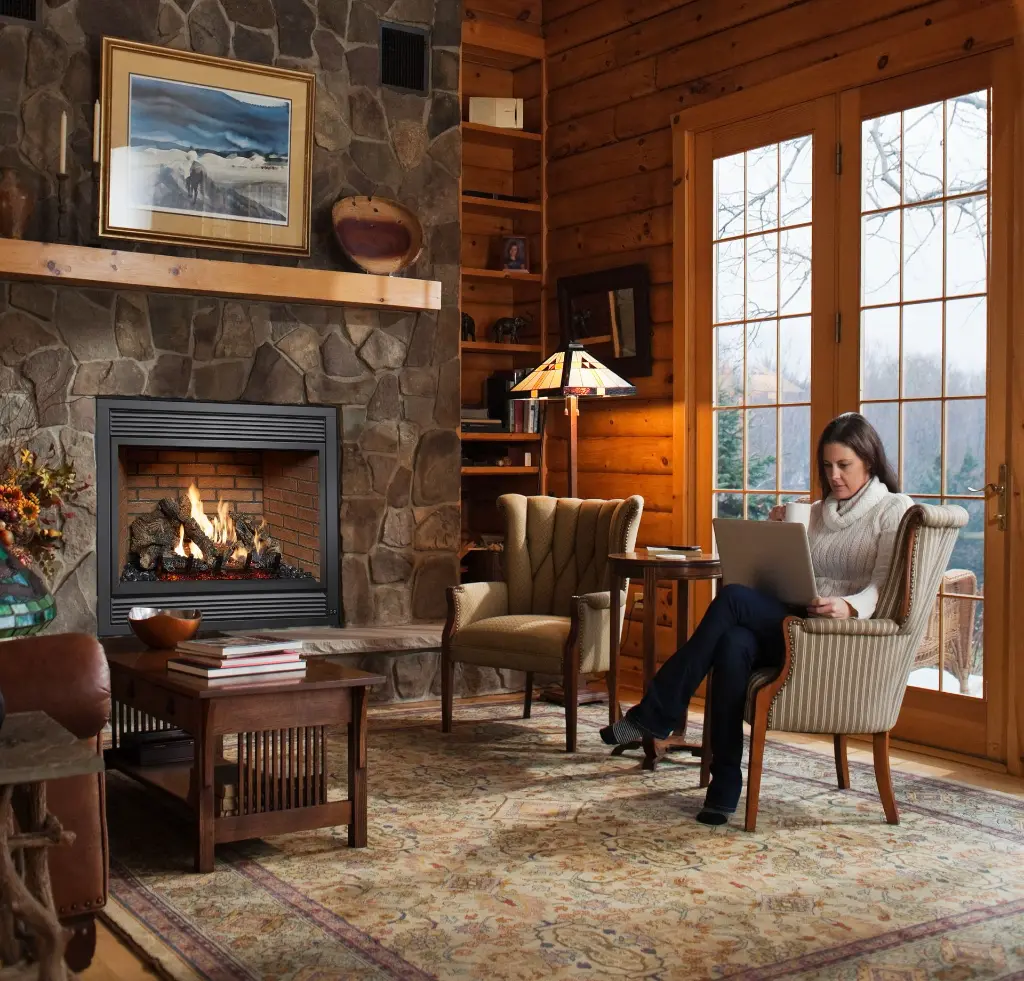 Foyer au gaz 864 TRV 31K offrant une ambiance chaleureuse dans un salon de style chalet, avec un manteau en bois brut et un mur en pierres empilées.