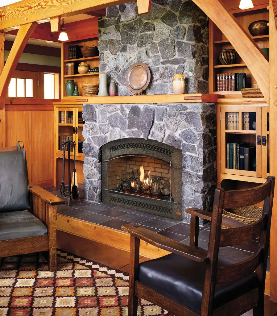 Ambiance de refuge rustique avec le foyer au gaz 864 TRV 31K, installé dans une cheminée en pierres de rivière et entouré de boiseries de style artisanal.