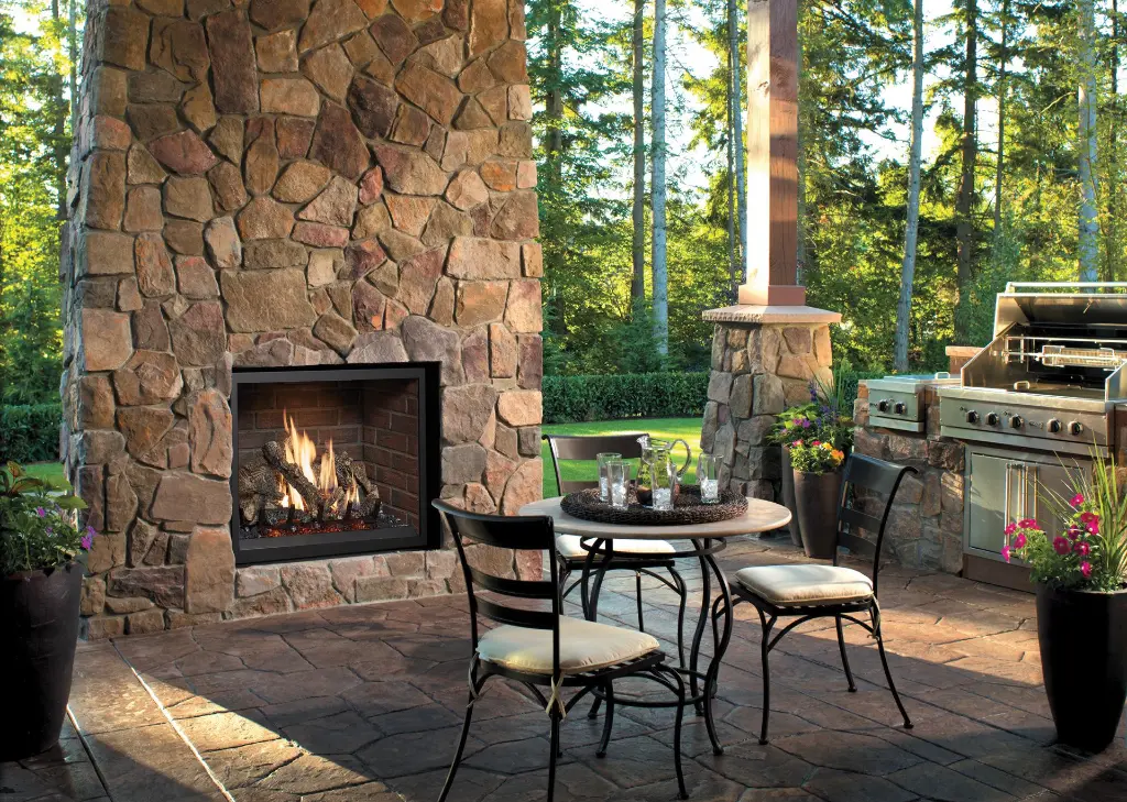 Aménagez une terrasse quatre saisons avec le foyer au gaz extérieur 864 TRV 31K, installé dans une cheminée en pierres des champs.