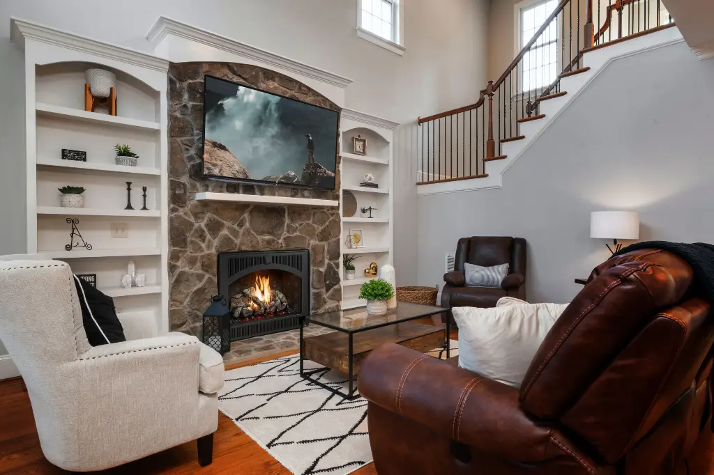 Centre de divertissement classique avec le foyer au gaz 864 TV 40K et sa façade arquée, intégré dans une cheminée en pierres et des bibliothèques blanches.