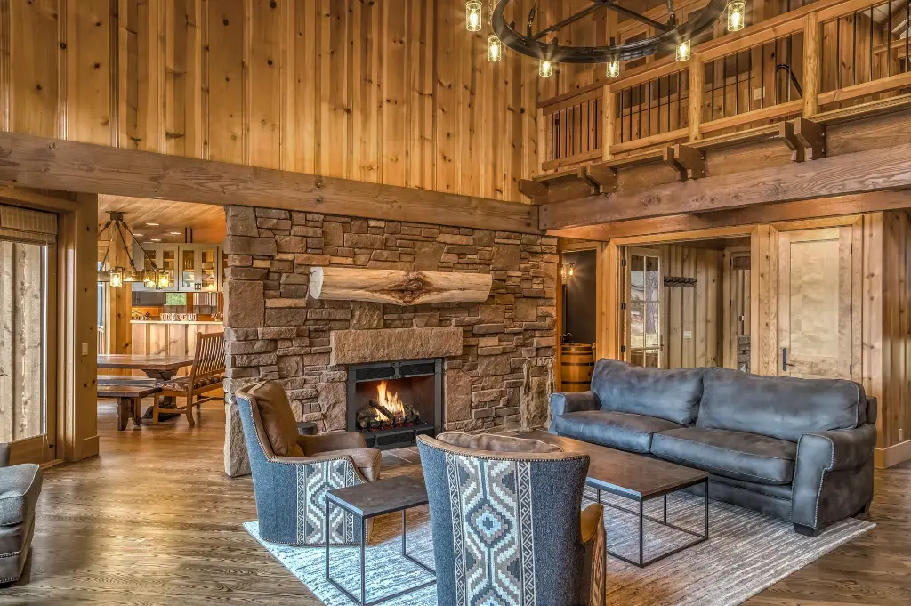 Ambiance de chalet de ski luxueux avec le grand foyer au gaz 864 TV 40K, intégré dans une cheminée en pierres et surmonté d'un manteau en bois brut.