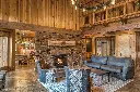 Ambiance de chalet de ski luxueux avec le grand foyer au gaz 864 TV 40K, intégré dans une cheminée en pierres et surmonté d'un manteau en bois brut.