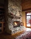 Look de chalet majestueux avec le foyer au gaz 864 TV 40K "Clean Face", encastré dans une cheminée en pierres des champs pleine hauteur.