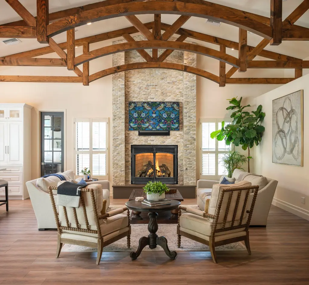 Grand salon avec plafond cathédrale et poutres de bois arquées, centré sur un foyer au gaz 4237 Ember-Glo dans une cheminée en pierres pâles.