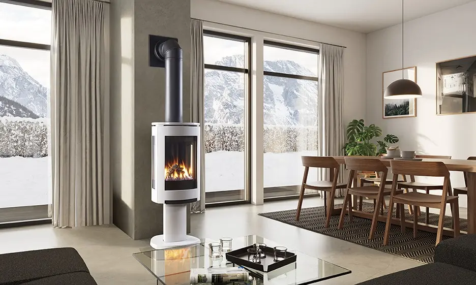 Poêle au gaz Jotul GF 370 noir mat sur piédestal, créant une ambiance chaleureuse dans un décor scandinave avec vue sur un paysage d'hiver.