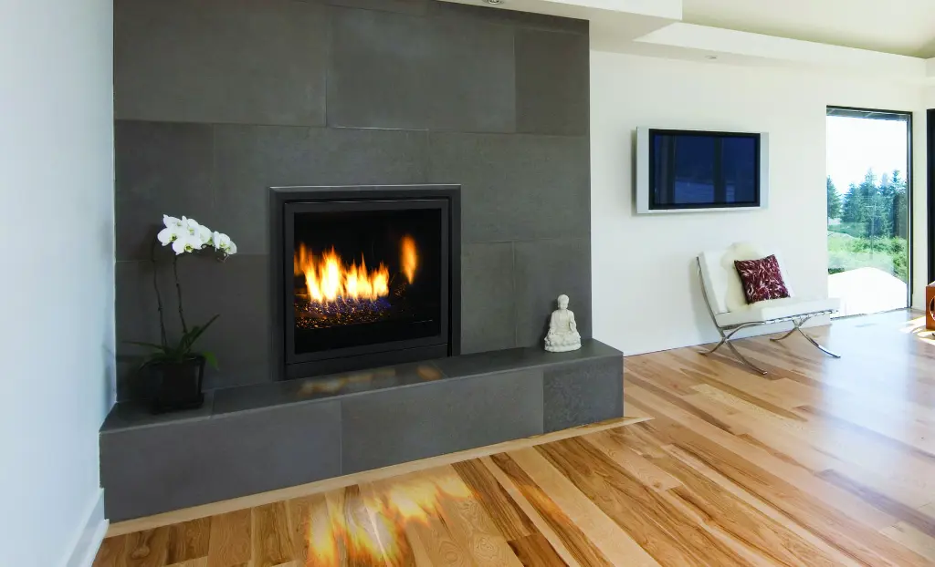 Installation moderne du foyer au gaz Enviro Q2, encastré dans un mur de grandes tuiles de porcelaine foncées avec un âtre surélevé.