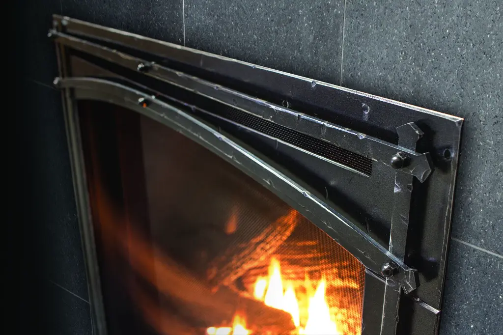 Gros plan sur les détails de la façade de style forge du foyer au gaz Enviro Q3, montrant le travail artisanal du métal et la grille de protection.