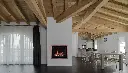 Foyer au gaz Sereno 37 d'Archgard avec un contour en cuivre, utilisé comme un séparateur de pièce architectural dans un espace à aire ouverte avec poutres de bois apparentes.