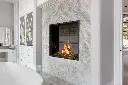 Ambiance de spa luxueuse avec le foyer au gaz Urbana U33, encastré dans un mur de marbre et créant une séparation avec une salle de bain principale.