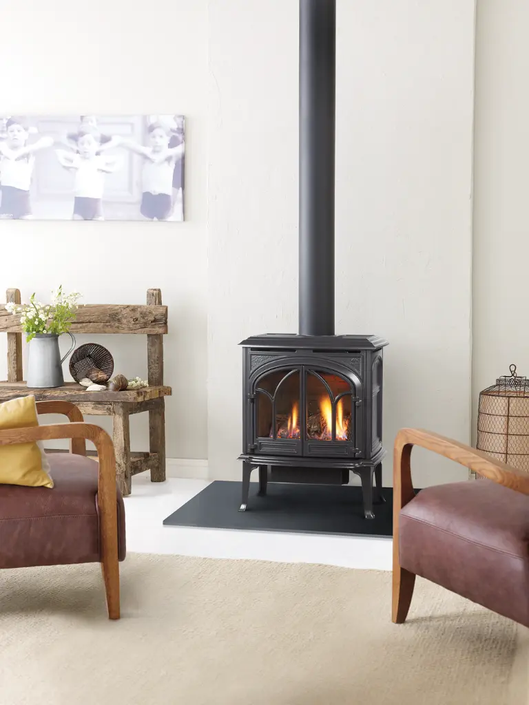 Poêle à gaz Jotul GF 300 noir mat sur pattes, créant un point focal dans un salon au style rustique moderne avec des fauteuils en cuir.