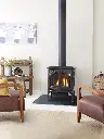 Poêle à gaz Jotul GF 300 noir mat sur pattes, créant un point focal dans un salon au style rustique moderne avec des fauteuils en cuir.