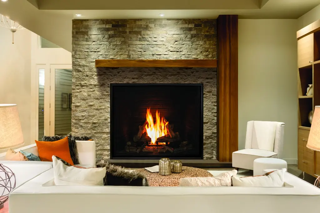 Ambiance de chalet moderne avec le foyer au gaz Urbana U55, encastré dans un mur de pierres décoratives et surmonté d'un manteau de poutre en bois.