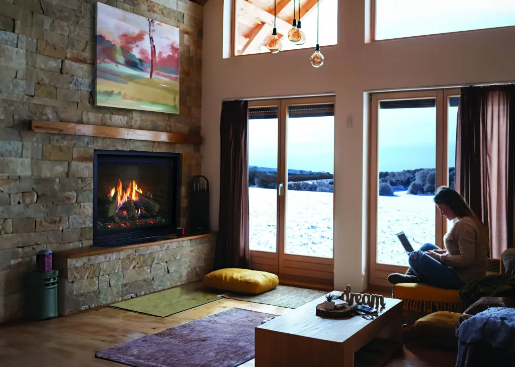 Ambiance de chalet moderne avec le foyer au gaz RZ41 d'Enviro, installé dans une cheminée en pierres décoratives avec une vue sur un paysage d'hiver.