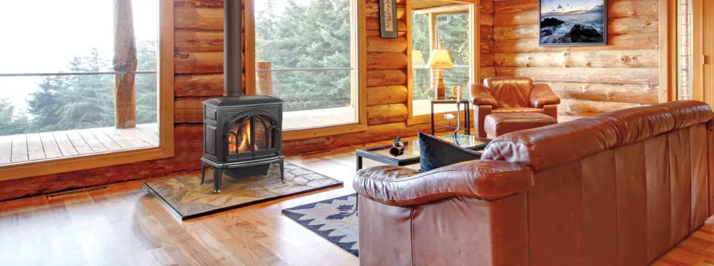 Poêle au gaz Jotul GF 400 noir mat, la pièce maîtresse d'un chalet en bois rond au décor rustique et luxueux avec vue sur la nature.