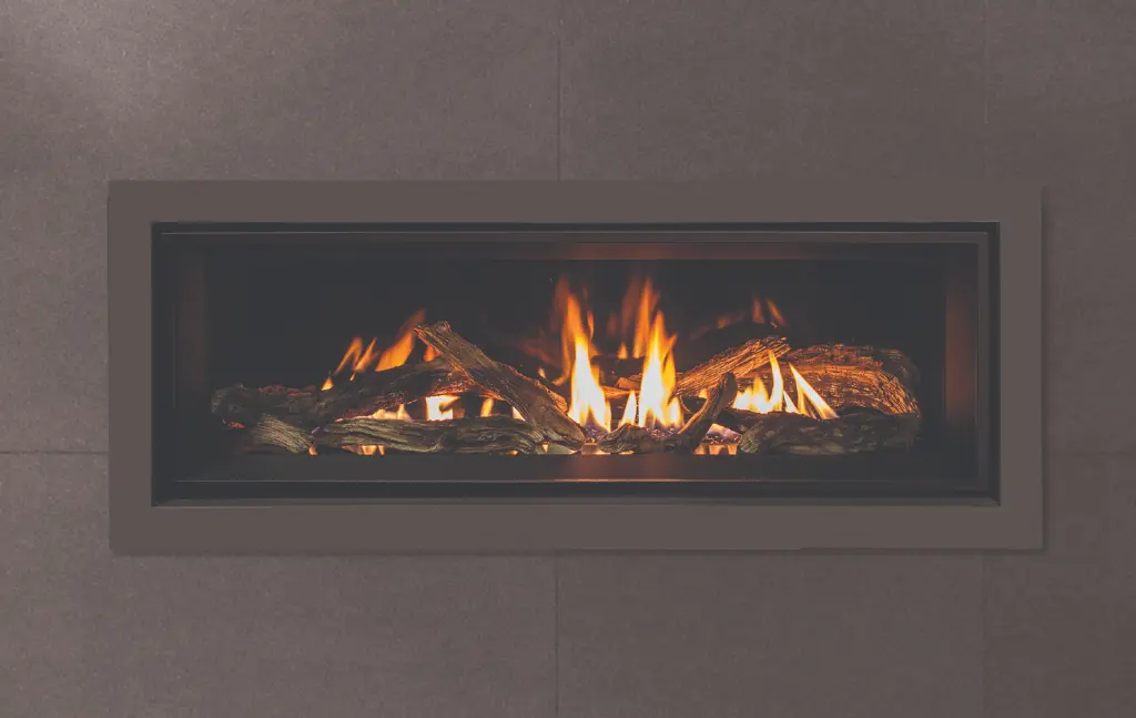 Vue de face du foyer au gaz linéaire Enviro C44 avec un contour noir mat, encastré dans un mur de tuiles grises foncées pour un look contemporain.