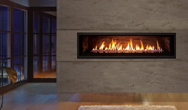 Ambiance intime et sophistiquée créée par la flamme d'un foyer au gaz linéaire Enviro C60, encastré dans un mur de béton ciré le soir.