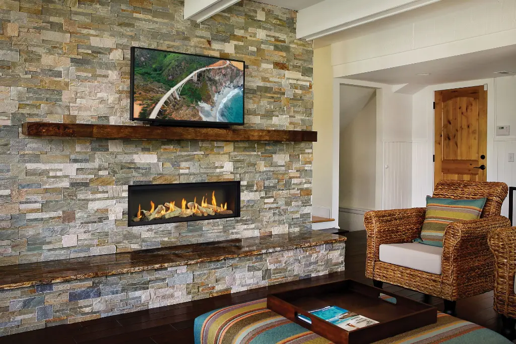 Ambiance de maison de plage avec le foyer au gaz linéaire 4415 HO, installé dans un mur de pierres naturelles pâles avec un manteau en bois brut.