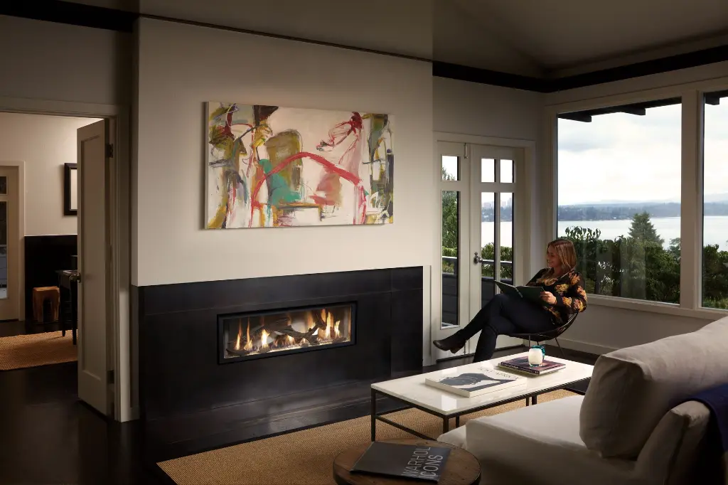 Ambiance sereine avec le foyer au gaz linéaire 4415 HO, installé dans un manteau de foyer noir pleine largeur avec vue sur l'eau.
