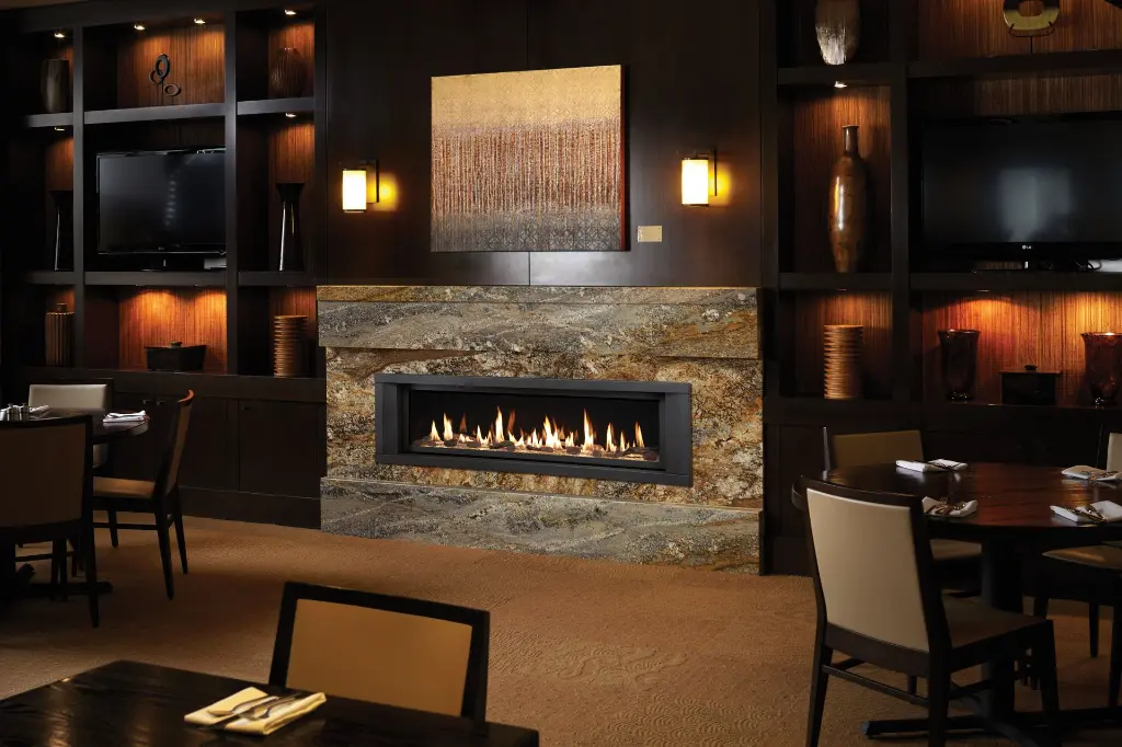 Look de restaurant lounge chic avec le foyer au gaz linéaire 6015 HO, intégré dans un manteau de foyer en granite et des boiseries foncées.