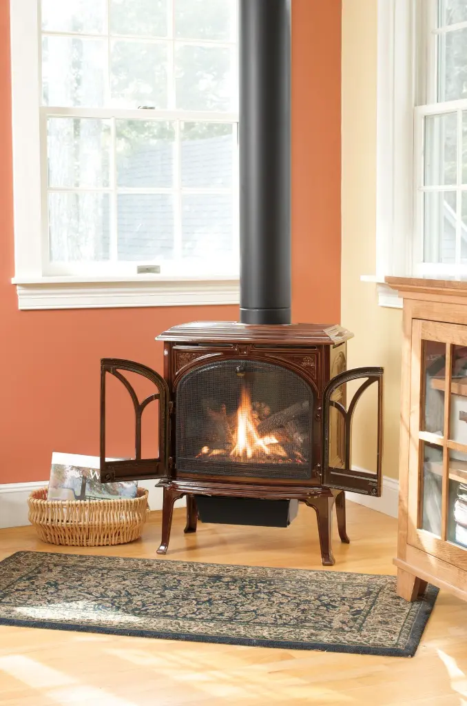 Poêle à gaz traditionnel Jotul GF 300 brun émaillé avec portes ouvertes, installé dans un coin lecture lumineux à côté d'une bibliothèque.