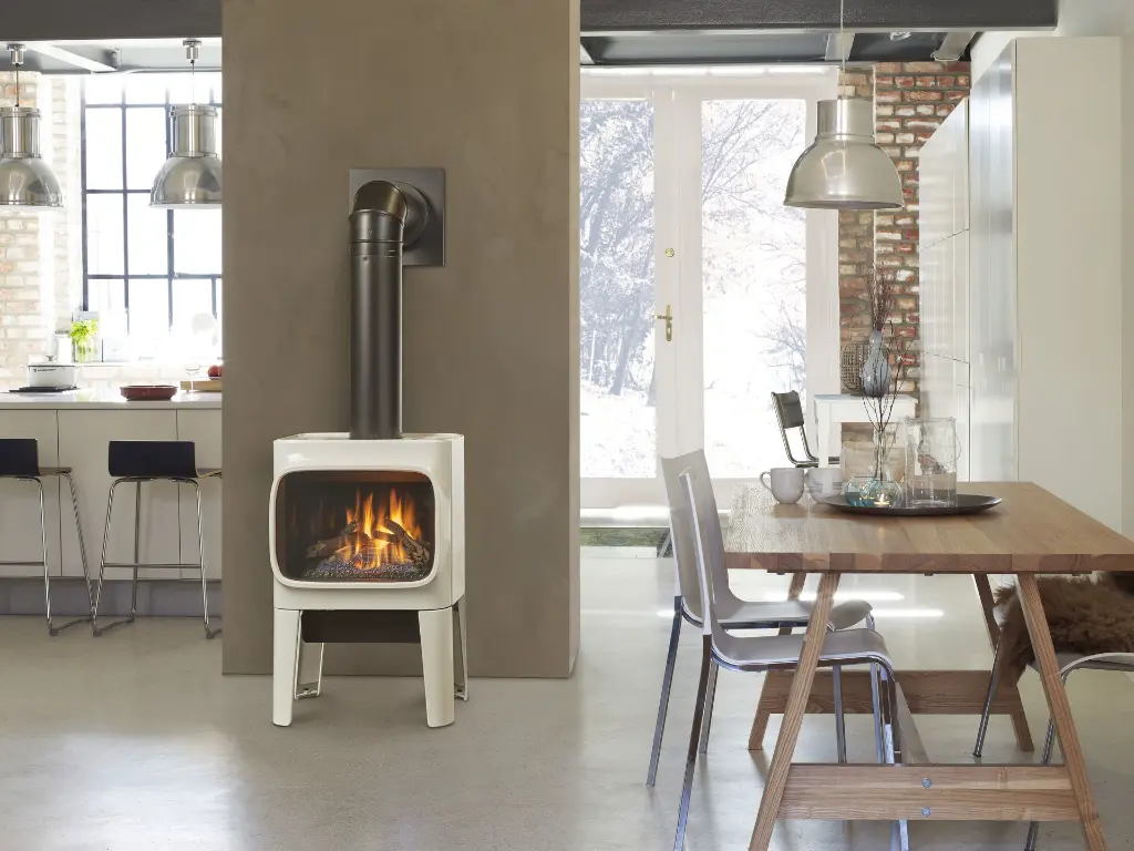 Poêle à gaz en fonte Jotul GF305 blanc émaillé, servant de séparateur de pièce entre une cuisine et une salle à manger dans un décor de style loft industriel.