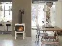 Poêle à gaz en fonte Jotul GF305 blanc émaillé, servant de séparateur de pièce entre une cuisine et une salle à manger dans un décor de style loft industriel.