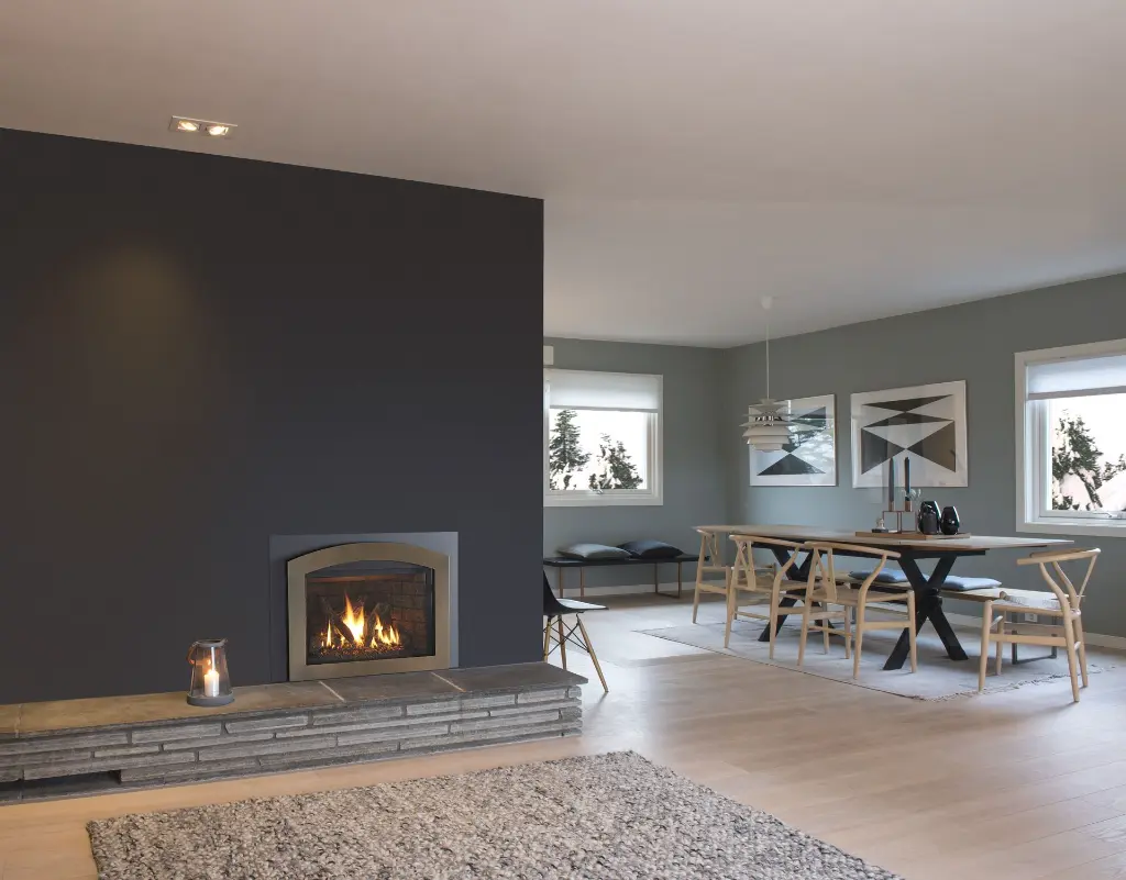 Insert au gaz Jotul GI 535 avec façade arquée en acier, créant un point focal dans un salon au design scandinave moderne avec un âtre en pierre.